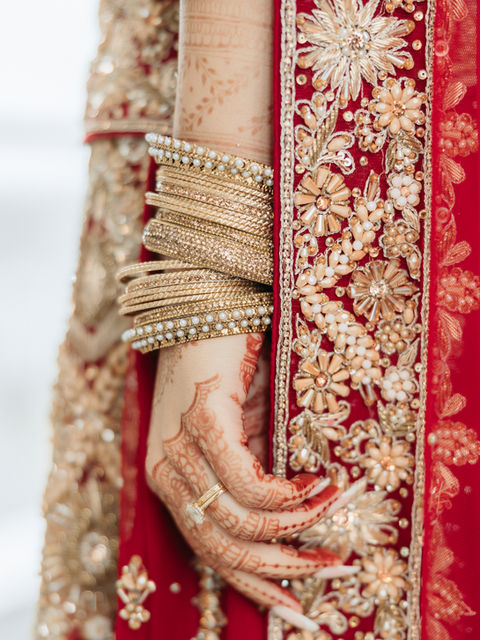 South Asian bride's hand with henna, gold bangles, red embroidery