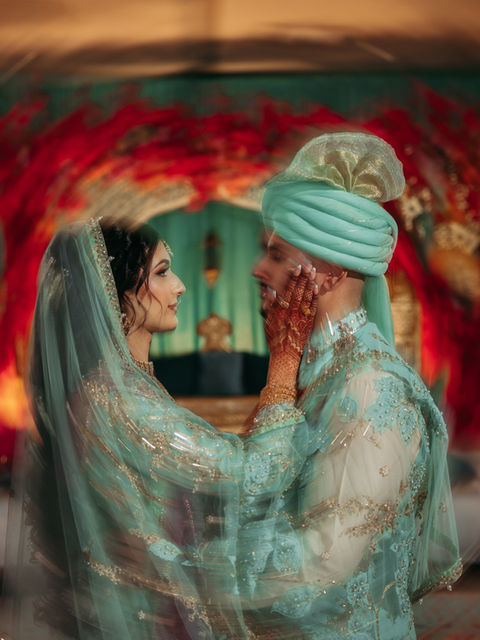 South Asian wedding couple in teal, woman touching man's face