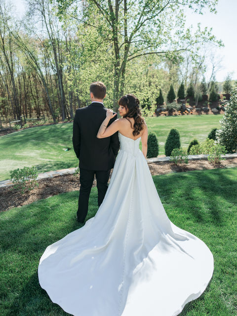 Bride in white dress with train next to groom, back to viewer