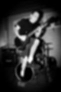 Black and white picture of Barclay playing guitar and jumping at a show.