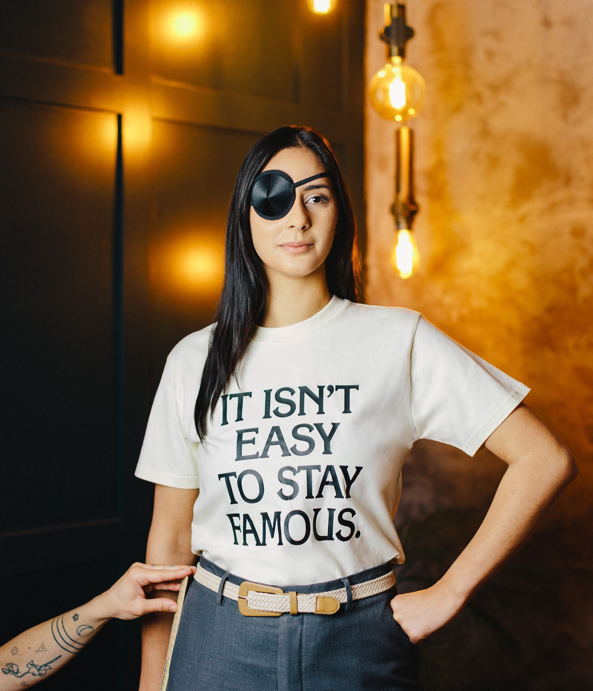 Woman wearing a white tee with a slogan, And wearing an eyepatch.