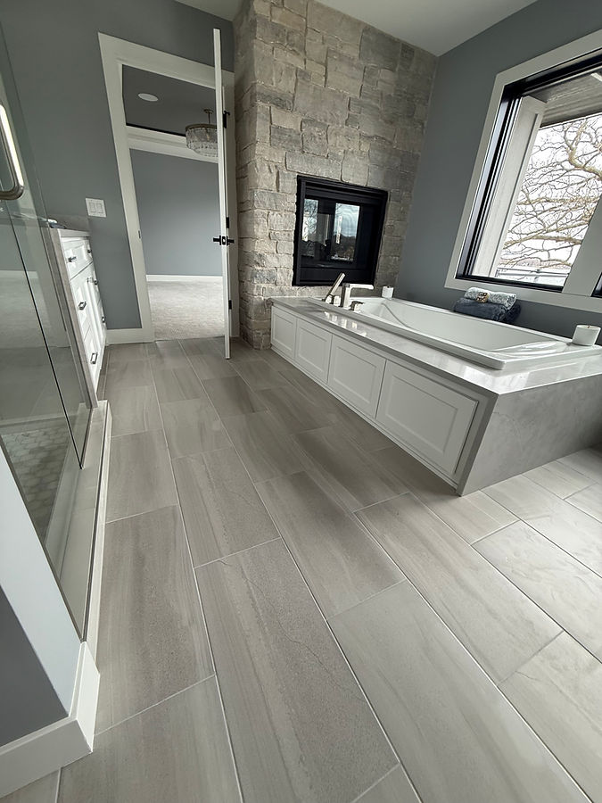 Custom heated tile flooring and stone fireplace in bathroom with large soaking tub