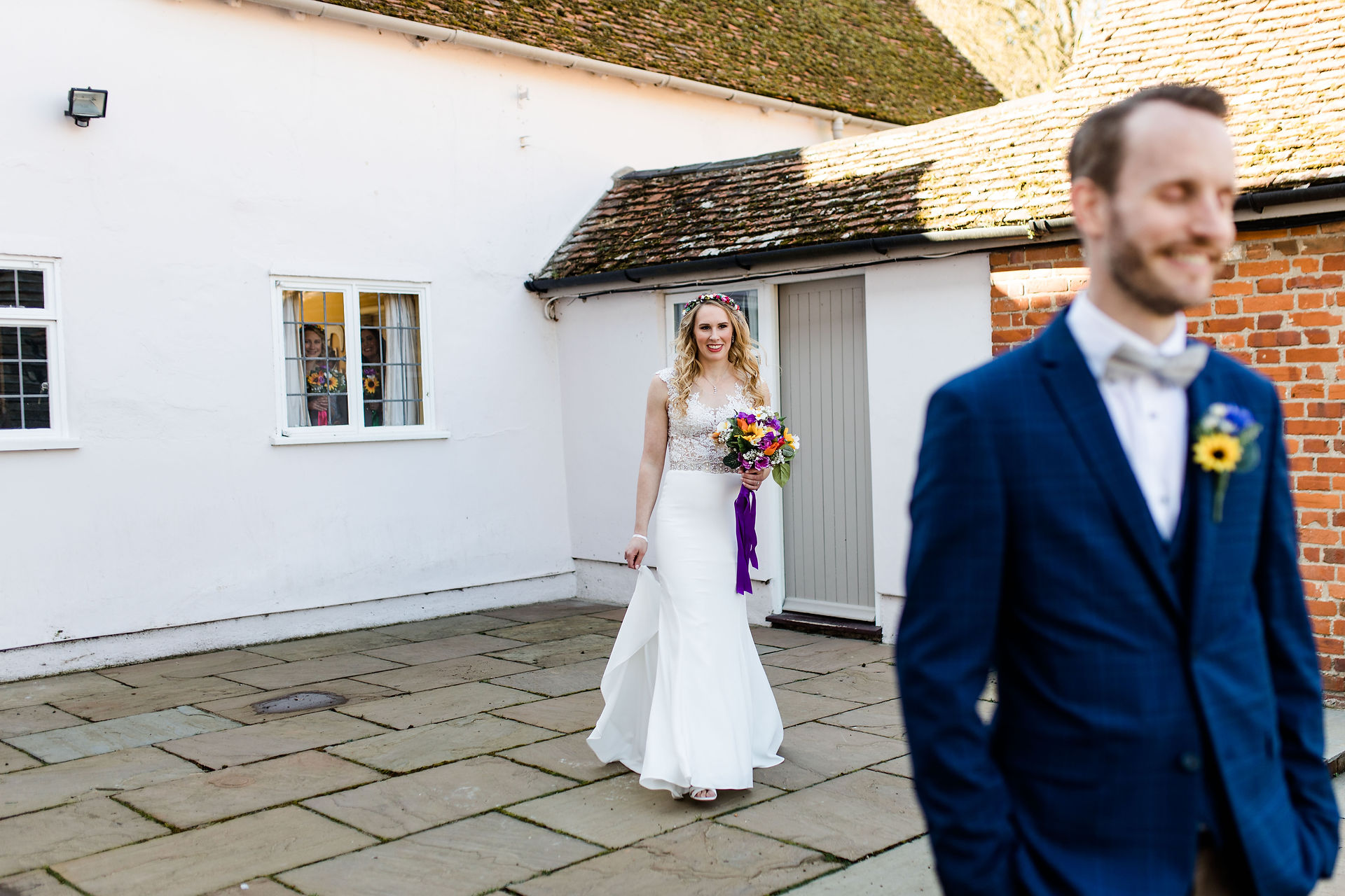 Bride with colourful bouquet walks towards the groom who stands with the back to her
