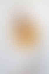 Blonde woman in white trousers and dark yellow top sitting on a bar stool, smiling