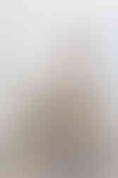 Blond woman with long hair sits on a chair , she is is wearing a white blouse and beige trousers