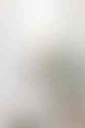 Blonde woman in a white suit holding an ipad, smiling and dancing in a bright room with a white sofa behind her