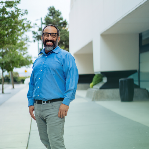 Smiling man standing on the sidewalk in front of a building.