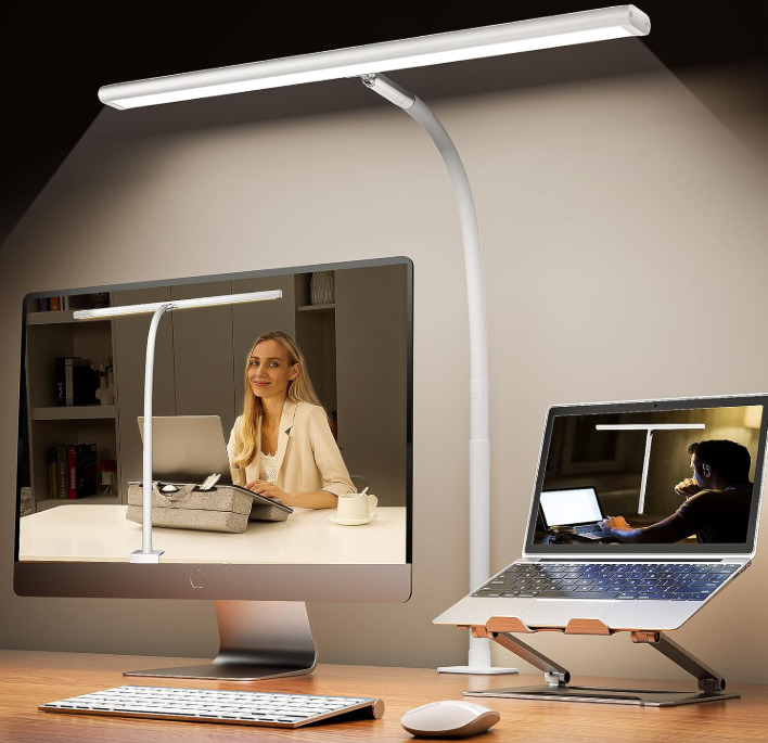 Dual white LED desk lamps illuminate a monitor and laptop showing people working at desks on a tidy office setup.