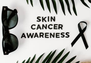 Siyah gözlükler ve kurdele ile çevrili "Skin Cancer Awareness" yazısı. Yapraklı zemin, sağlık farkındalığı vurgusu.