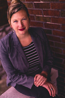Our club advisor, Lydia Paar. White woman, blonde hair, posing in a sitting position, smiling.