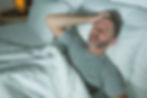 Homem de meia-idade deitado na cama com expressão de cansaço e dor de cabeça, sugerindo má qualidade do sono ou distúrbio como apneia do sono.