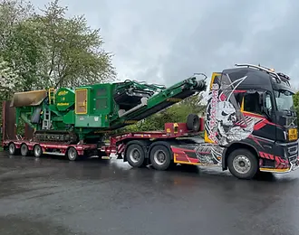 Un camion trak trans transportant sur sa semi porte-engins (ou porte-chars), un engin lourd et volumineux.