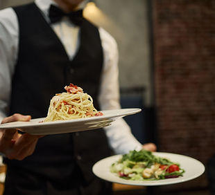 Caucasian young adult waiter serving pasta and salad in restaurant, presenting dining serv