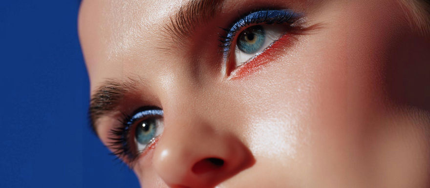 Close-up of bold makeup with vibrant blue eyeshadow, red lipstick, and glowing complexion, highlighting modern fashion trends.