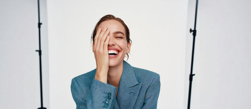 A joyful person in a blue blazer, laughing and posing against a simple background.