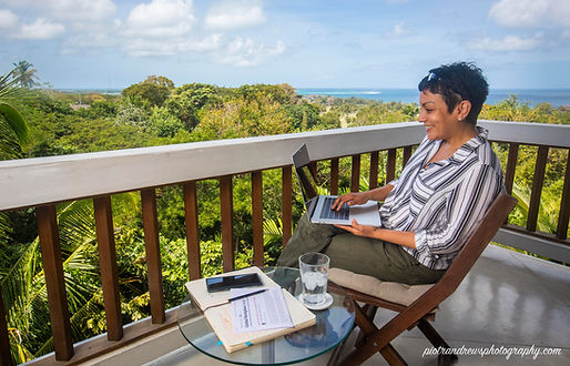 Businesswoman works remotely on her laptop from a balcony of an apartment with a view to the Caribbean Sea in Tobago