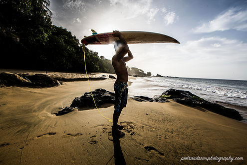 A young man holds his surfboard above his head on the beach in Tobago