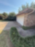 Driveway and garage entrance of a home with a green lawn and trees.