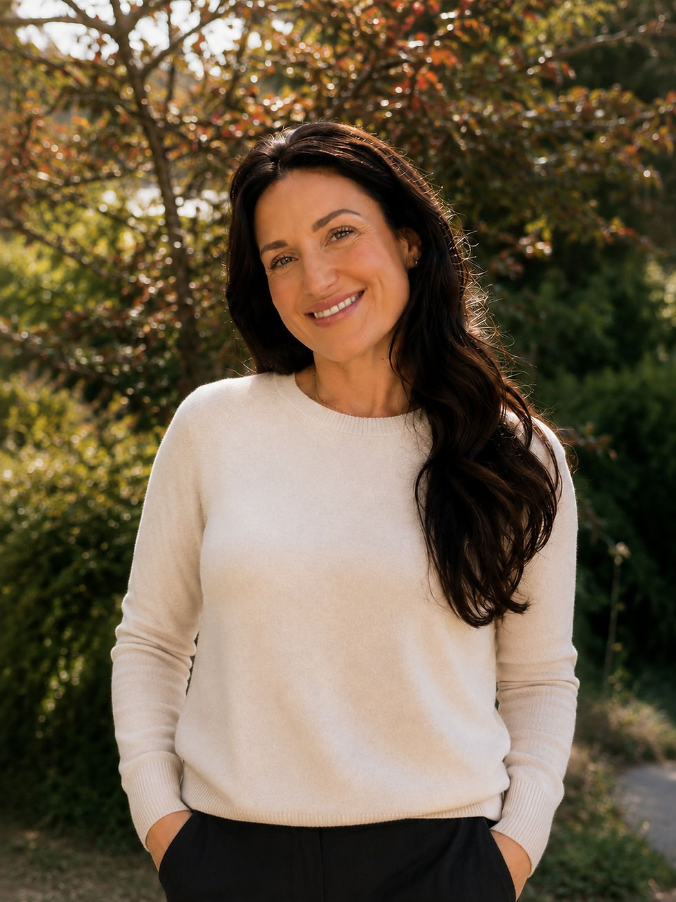 Picture of a woman smiling in a sweater outside with a warm autumn background.