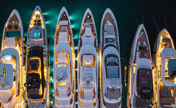 yachts all tied together in a row at boat show at night time with lots of lights on the bo