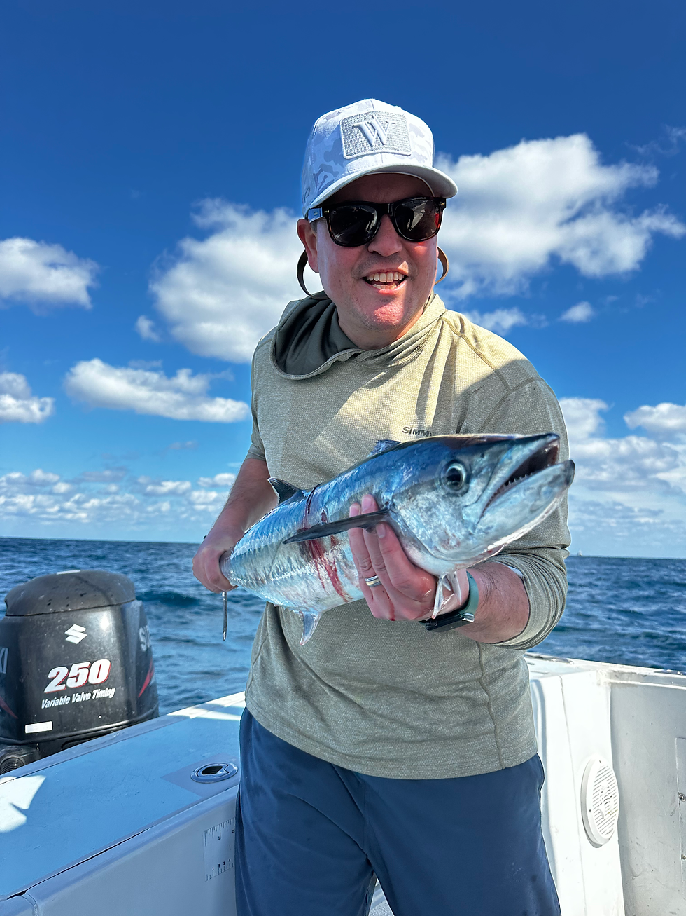 Man in sunglasses and a cap holding a large fish on a boat under a bright blue sky with clouds. Engine shows "250 Suzuki." He appears happy.