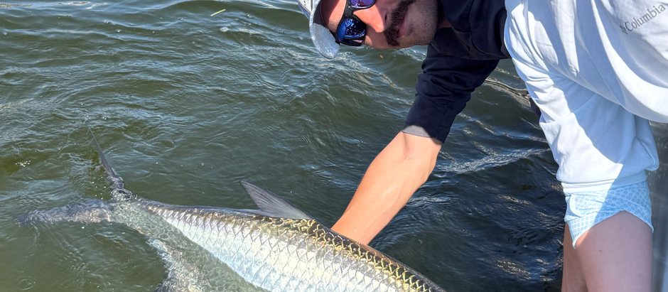 one man and one boy leaning over the side of the boat close to the water while holding a tarpon for a picture