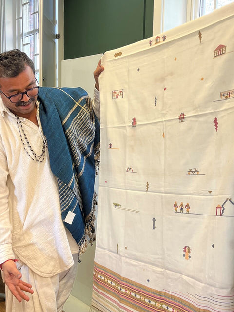 man dressed in traditional Southeast Asian clothing illustrates a piece of hand-woven cloth