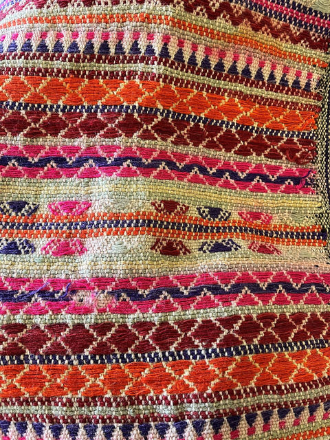 detail of a piece of hand-woven fabric with geometric decorations and bright colors such as purple fuchsia red orange and white