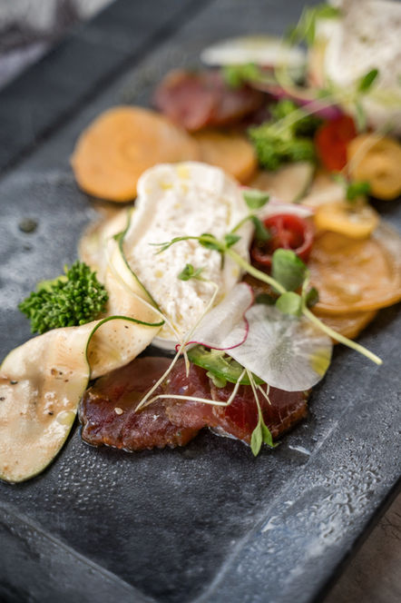 Plated appetizer with cured meat, creamy cheese, and herbs.