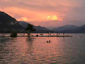 People swimming in lake Annecy as the sun goes down. The sky is pink and purple.