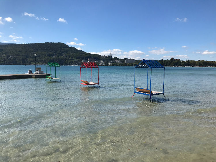 Two brightly coloured sun bathing platforms made from metal and wood sit in lake Annecy but they are emply because it is too hot.
