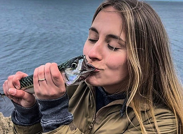 Young lady kissing the fisrts fish she's ever caught, a mackerel , a kiss before smoking it for supper!