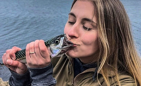 Young lady kissing the fisrts fish she's ever caught, a mackerel , a kiss before smoking it for supper!