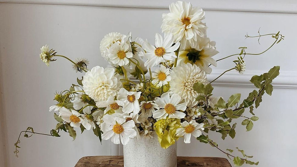 White wildflowers arranged in a minimalist ceramic vase on a rustic wooden stool, symbolizing a clean, natural home environment.