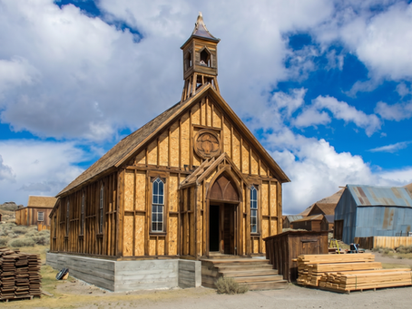 Historic wood-frame church undergoing structural restoration in a rural California setting, with lumber and building materials staged on site.