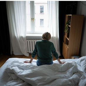 A woman sits on an unmade bed looking despondent