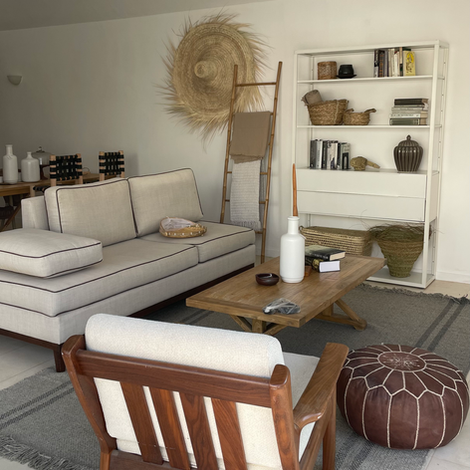 ספה לבנה עם כריות, שולחן קפה מעץ, כיסא מעץ, סולם מעץ, מדף ספרים לבן עם סלים, שטיח אפור וחום, קישוט קיר מעשה יד