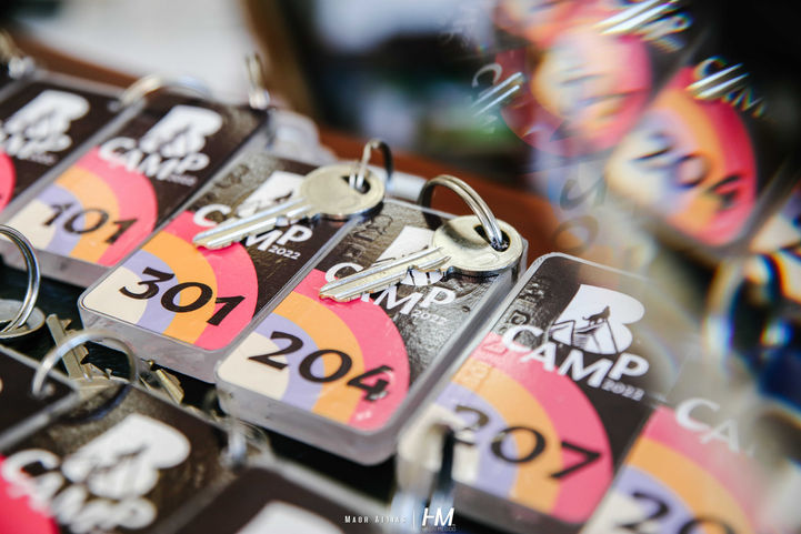 תקריב של מחזיקי מפתחות ממותגים עבור אירוע BRITANIKA ✦ Camp. כל מחזיק מפתח כולל את לוגו האירוע עם איורי ההרים והיער ומספר חדר או אוהל ייעודי (כמו 301, 204, 101). הצילום הממוקד מדגיש את המעבר מחיי היומיום לחוויית אירוח מלאה בסטנדרט של מלון בוטיק בלב הטבע. הפקה: חגי מגידו – HM Productions.
