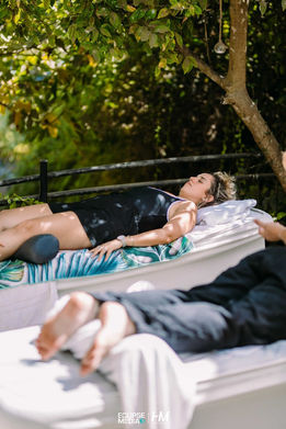 משתתפת באירוע החברה Breathe ✦ Intango נחה במצב של רגיעה עמוקה על מיטת שיזוף מעוצבת. היא שוכבת תחת צל העצים בגינה ירוקה, משתמשת בכרית תמיכה לרגליים ובכיסוי עיניים כדי למקסם את חוויית הניתוק והשלווה. הפקה: חגי מגידו – HM Productions.