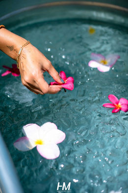 תקריב על יד המניחה בעדינות פרחי פלומריה (פיקוס קדוש) ורודים ולבנים בתוך קערת מים צלולים, כחלק מעמדת אווירה או ספא באירוע Drive-net ✦ Club. הצילום משדר רוגע, אסתטיקה וחיבור לאווירה הטרופית של האירוע. הפקה: חגי מגידו – HM Productions.