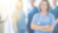 Smiling woman nurse with arms crossed facing the camera. A team of nurses standing behind her.
