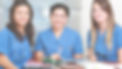 Three women nurses sit together around a table smiling