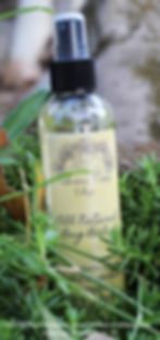 Closeup of tall, round bottle of bug balm in greenery.