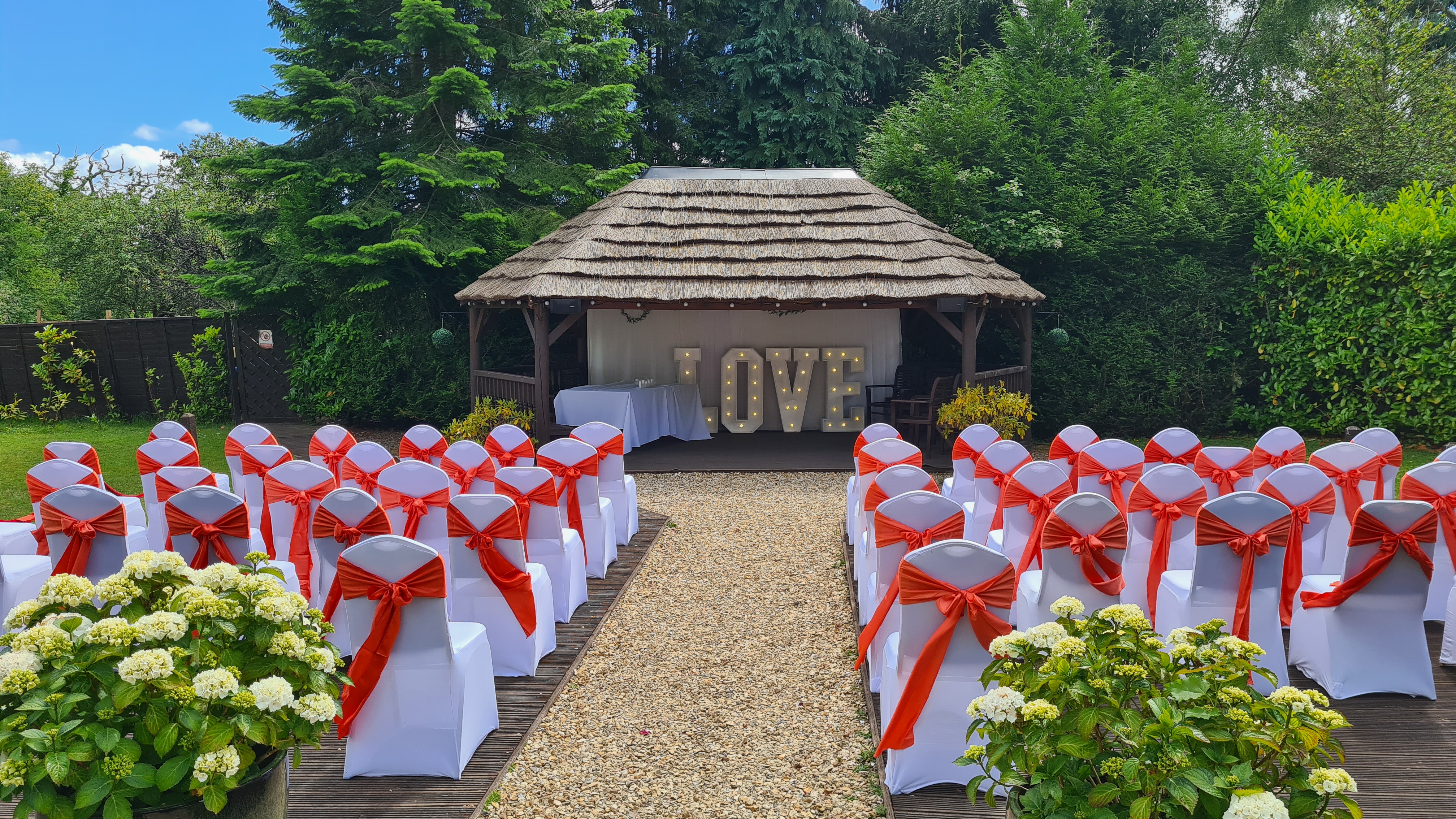 Outdoor wedding ceremony setup: LOVE sign, white chairs with red sashes