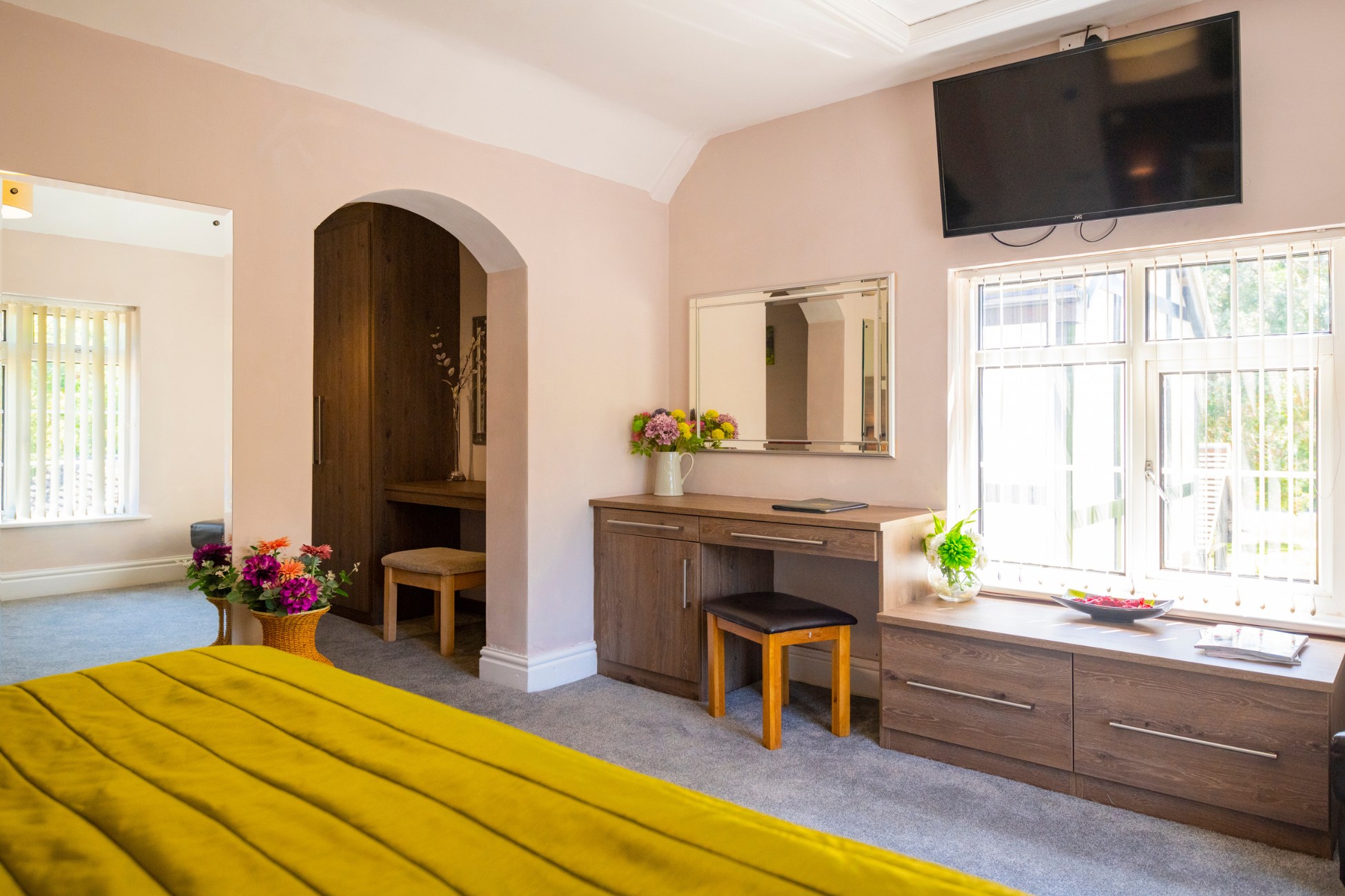 Spacious bedroom with yellow bedspread, dressing table, and TV