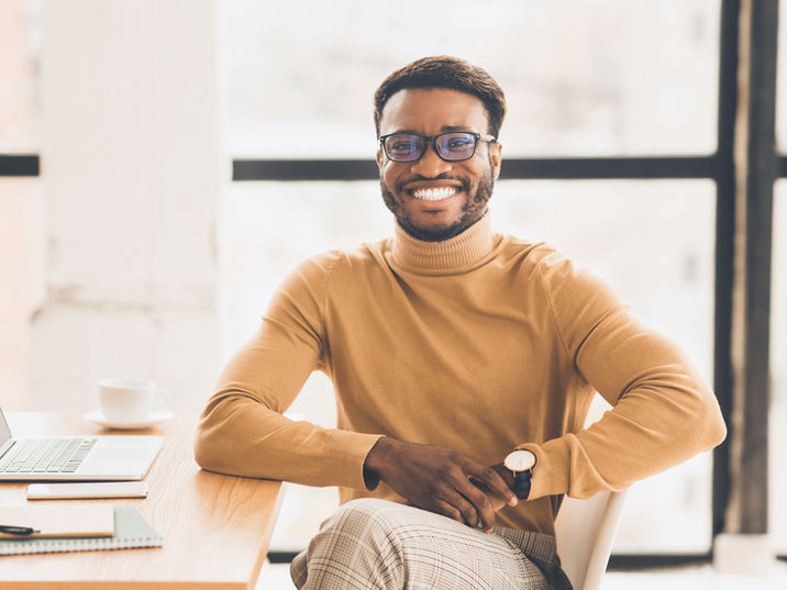 Smiling Black man in glasses at a desk with laptop