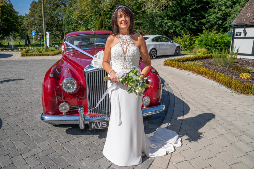 Bride in wedding dress with bouquet by classic red car