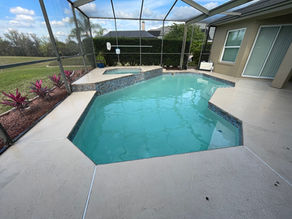 Modern backyard pool with blue tile accents, screened enclosure, adjacent hot tub, and garden. Bright sky visible through the enclosure.