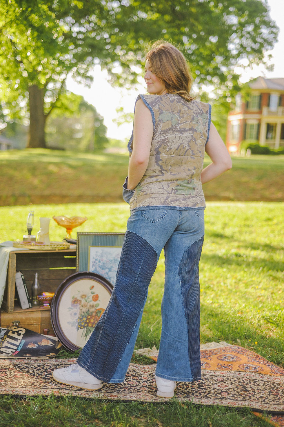 Thumbnail: A woman stands barefoot on a vintage rug outside, wearing high-waisted flared jeans with dark blue corduroy inserts on the le