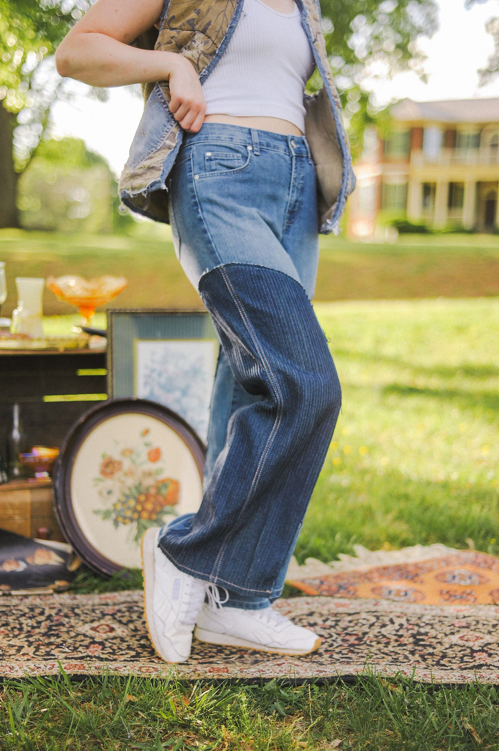 Thumbnail: A woman stands barefoot on a vintage rug outside, wearing high-waisted flared jeans with dark blue corduroy inserts on the le